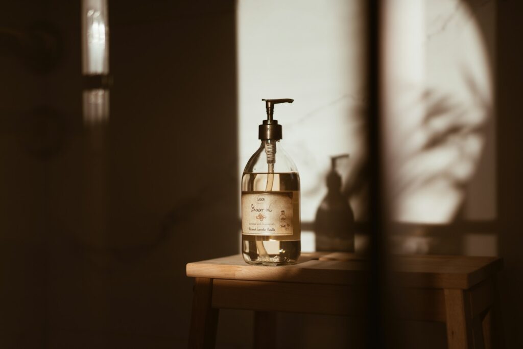 Shower-oil pump bottle on a wooden stool in warm autumn light