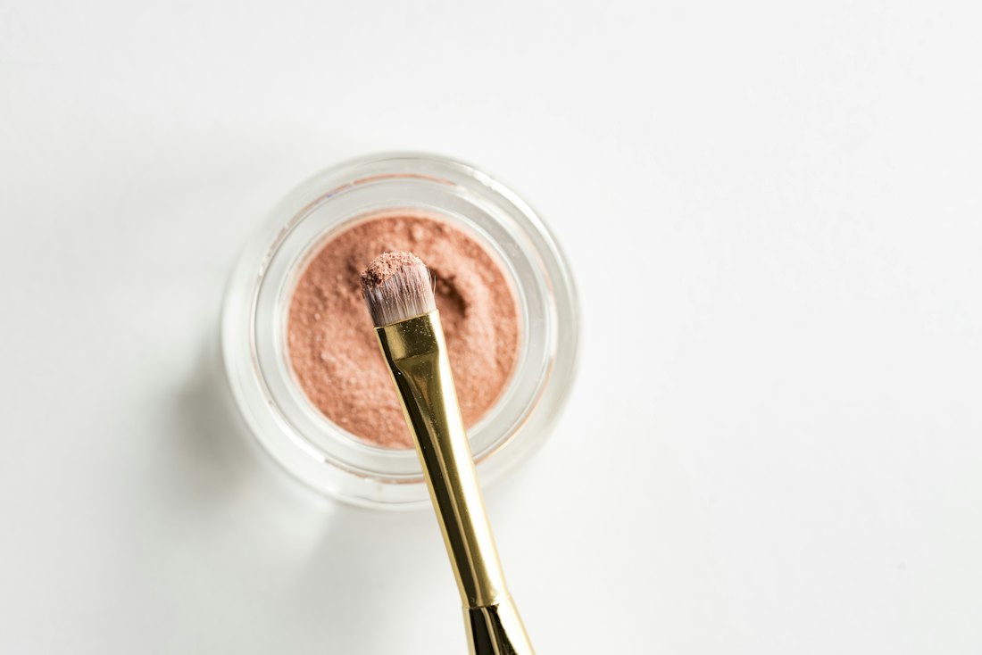 Makeup brush resting over a pot of peach-colored loose cosmetic pigment