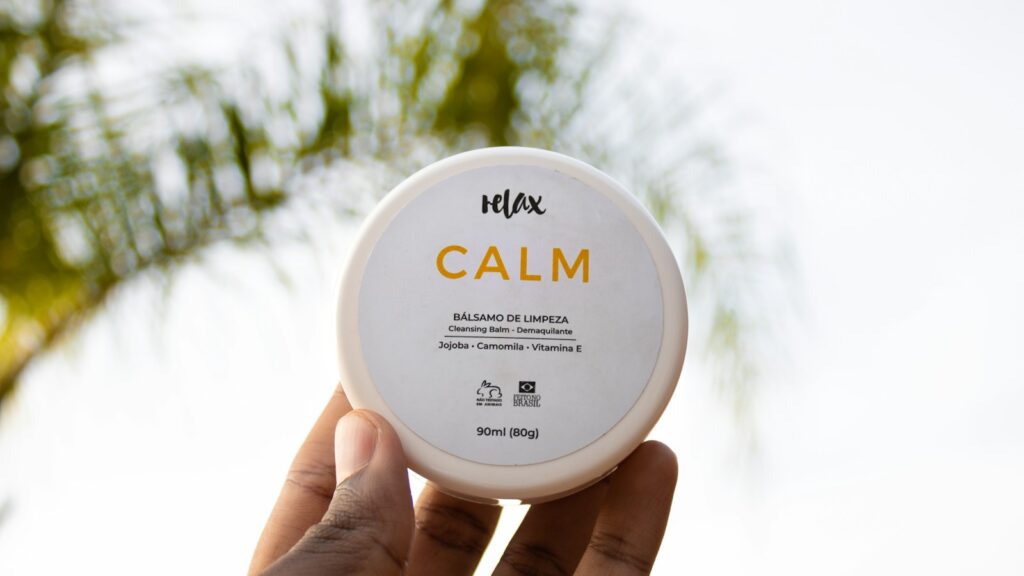 Hand holding a closed jar labeled cleansing balm in natural light