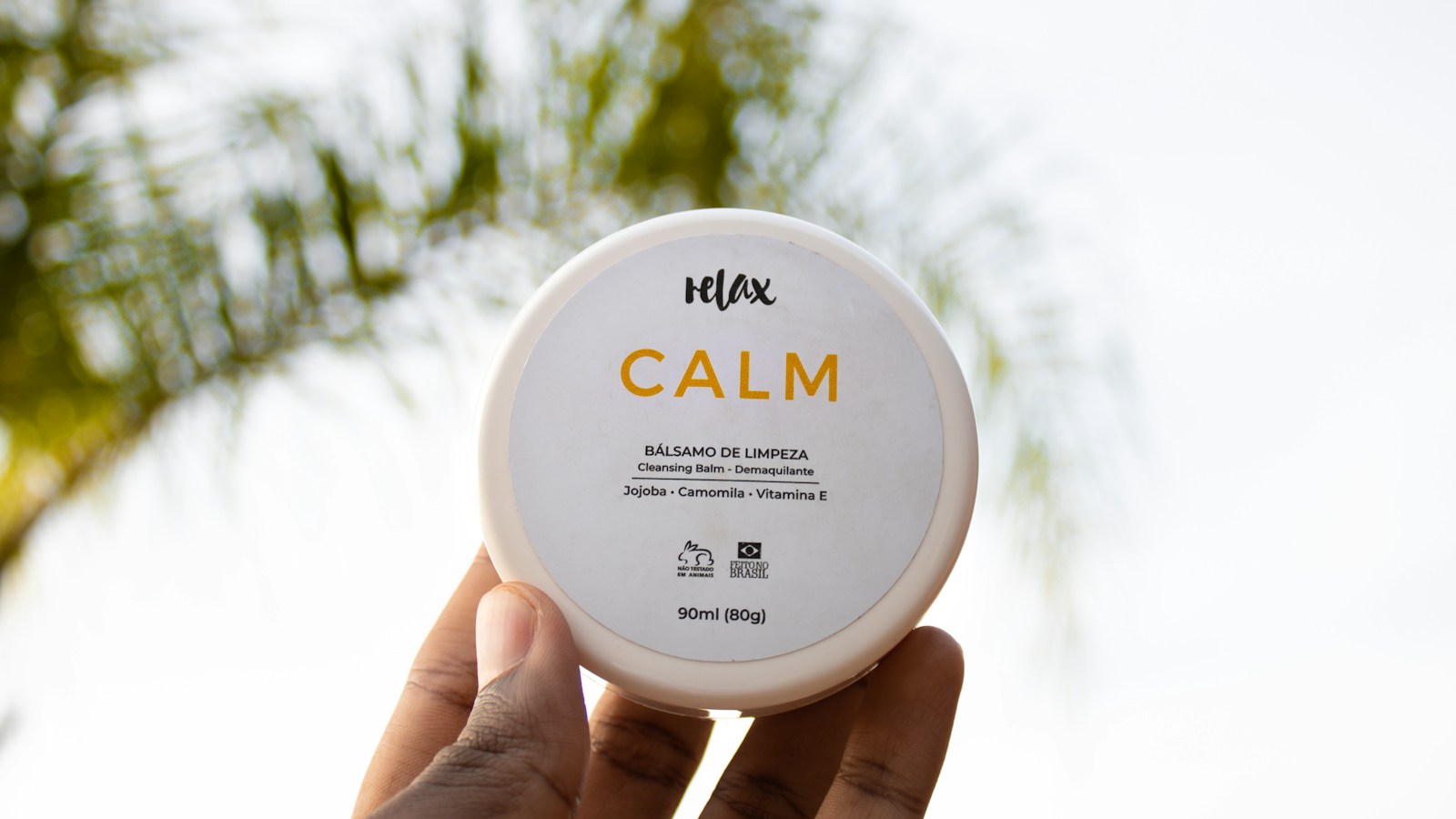 Hand holding a closed jar labeled cleansing balm in natural light