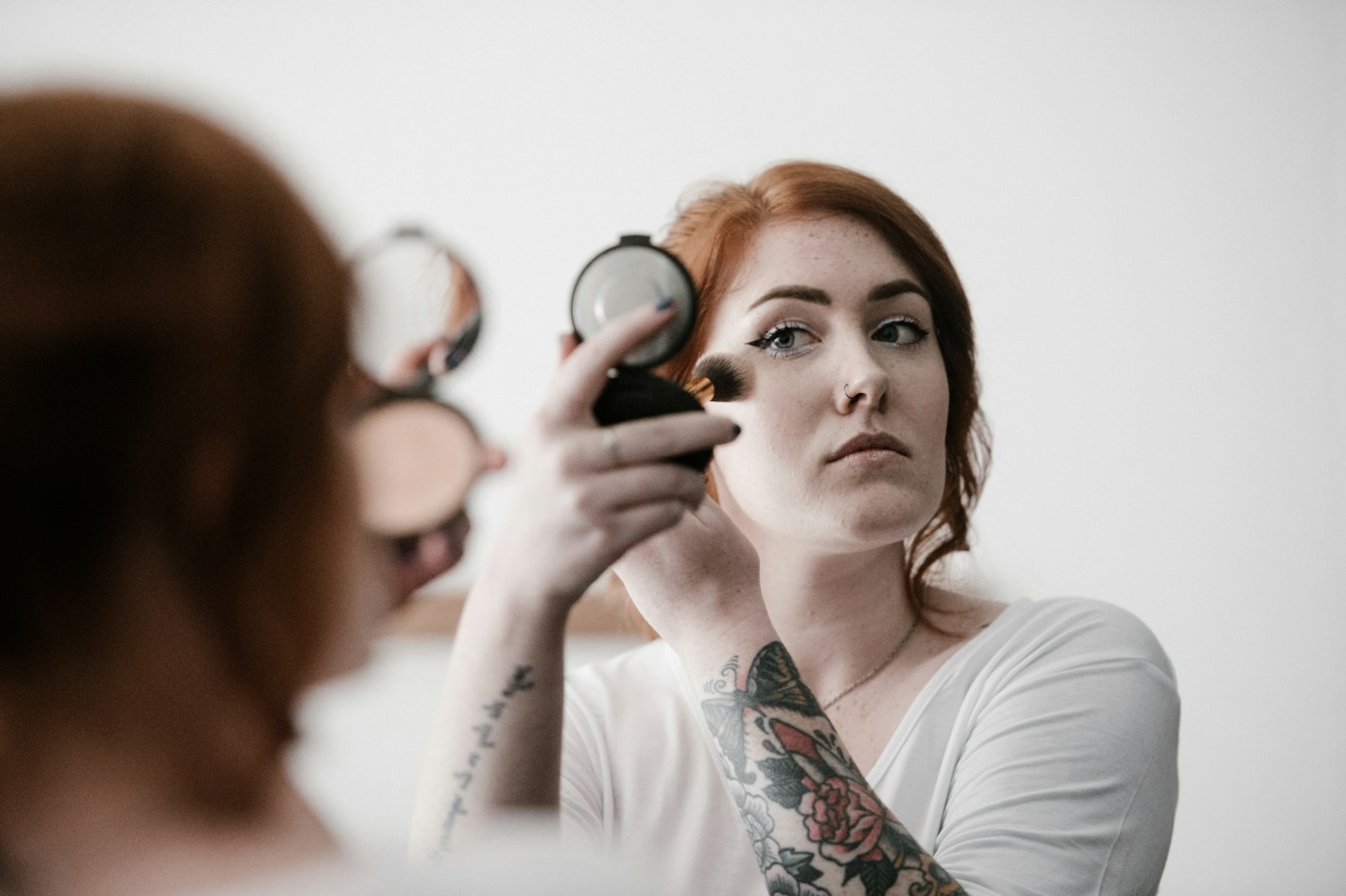 Woman using a face brush while looking into a compact mirror